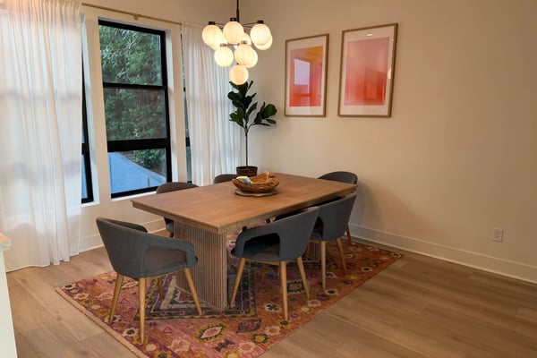 Dining room with wooden table, gray chairs, pendant light fixture, potted plant, and framed artwork on walls